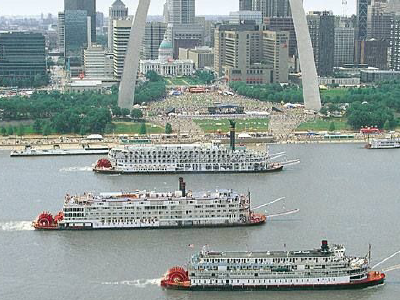 Three large riverboats racing on the Mississippi River in front of the Gateway Arch.