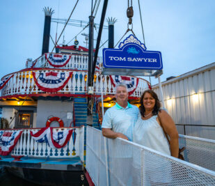 A couple poses for a photo in front of the Tom Sawyer riverboat before a Skyline Dinner Cruise.