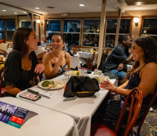 Three women laughing and chatting while they eat on a Skyline Dinner Cruise.