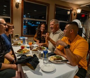 A family laughing and chatting while they eat on a Skyline Dinner Cruise.